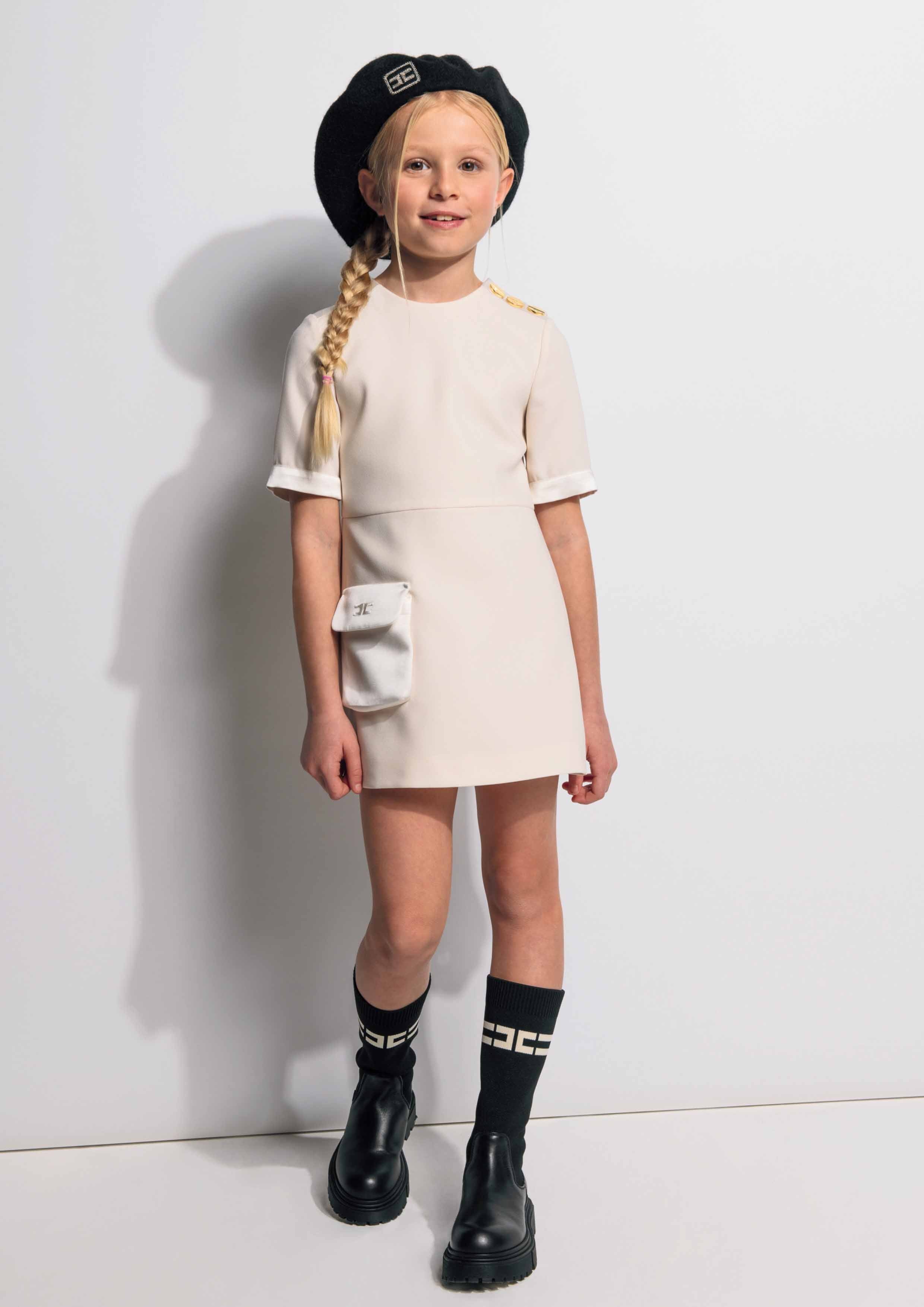Young girl in a white dress with black boots and hat against a white background